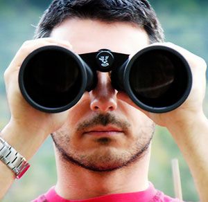 Photo of a man looking through binoculars, signifying the importance of looking ahead in your college search. Here are five things to know before applying to college