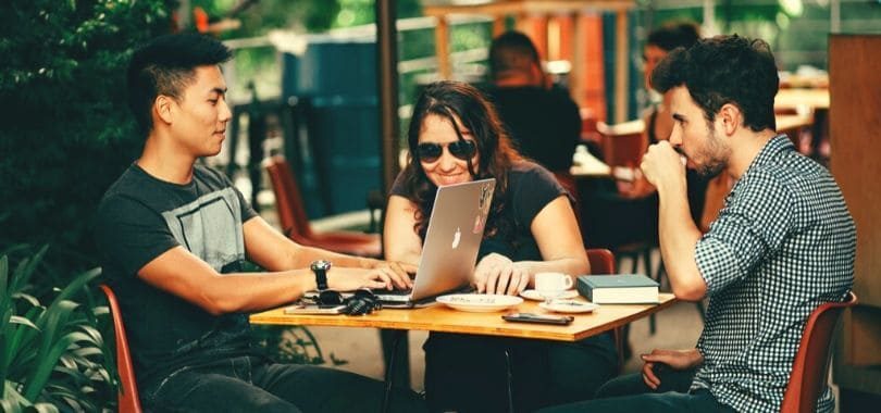 Three students sitting at a table, with a laptop and notebooks on the table.