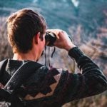 A student looking through a pair of binoculars.