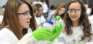 Two women wearing lab gear performing a science experiment.