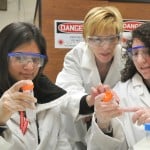 3 women wearing laboratory dress and eye protection.