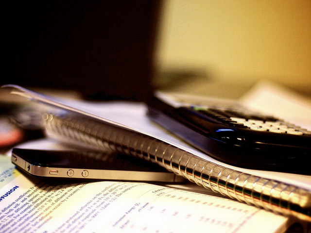 Books, cellphone, notebook and calculator piled up.