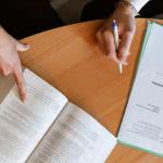 A school counselor pointing at a book while a student takes notes.