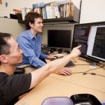 College professor pointing to the monitor while his student is navigating the computer.