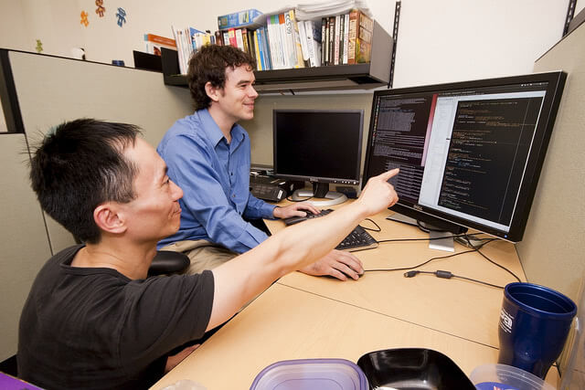College professor pointing to the monitor while his student is navigating the computer.