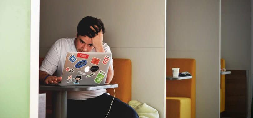 A high school student sitting with their laptop, looking frustrated.