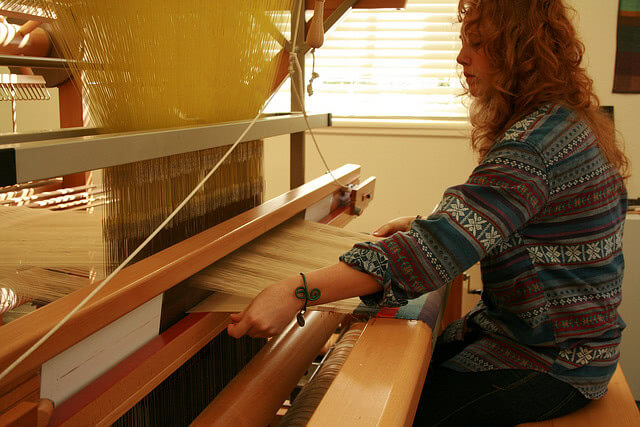 A lady knitting fabric using a manual machine.