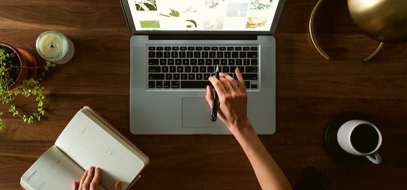 A student typing on a laptop with one hand, and writing down notes with the other.