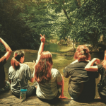 Five students sitting together on a log over a river.