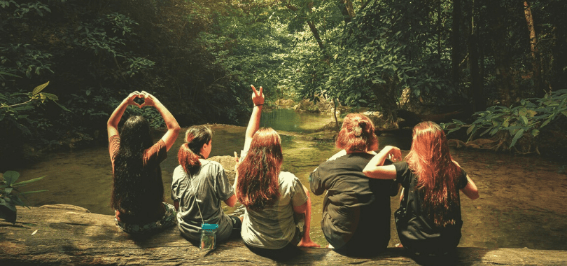 Five students sitting together on a log over a river.