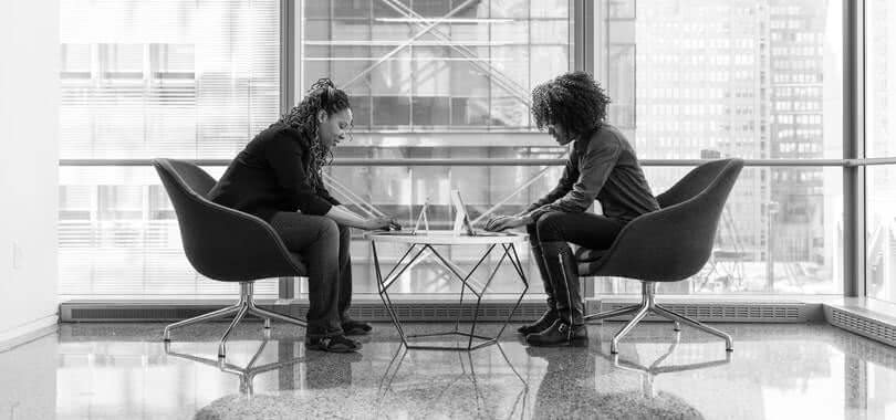 Two college counselors sitting together on their laptops.