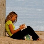 Photo of a girl reading a book on the beach.