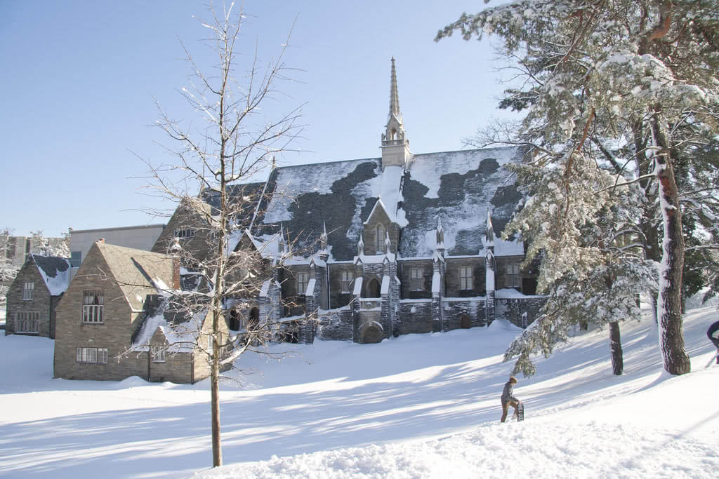 A student hiking through the snow in front of a Bryn Mawr College building.