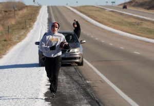 A college student running while other students cheer him on in a car from behind.