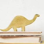 A wooden dinosaur on top of a stack of books.