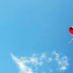 A red heart balloon floating against a blue sky.
