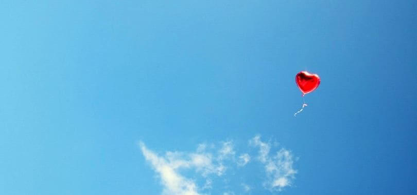 A red heart balloon floating against a blue sky.