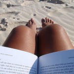 A teacher reading a book at a sandy beach during summer.