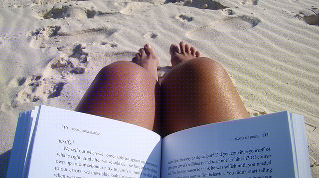 A teacher reading a book at a sandy beach during summer.