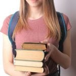 A student holding a stack of books with both hands.