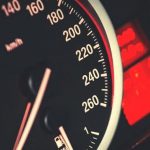 A black and red speedometer with a red light next to it.