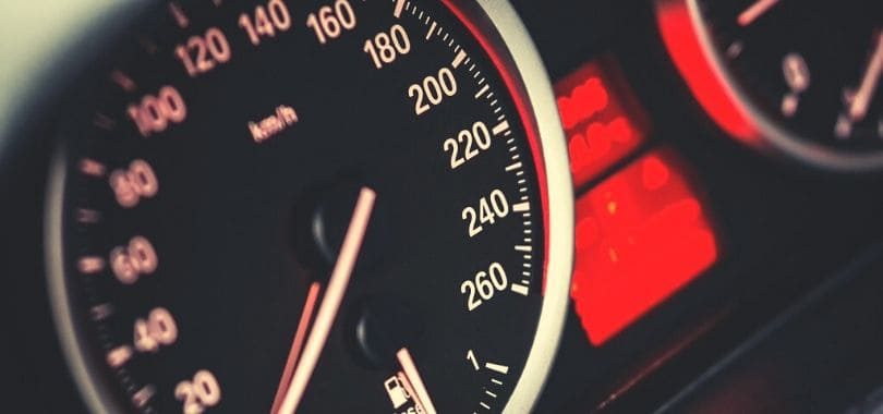 A black and red speedometer with a red light next to it.