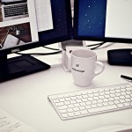 Dual Dell monitor on a desk with white coffee cup.