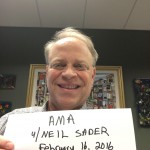 A man holding a paper that says "AMA with Neil Sader February 16, 2016 at 10 am ET".