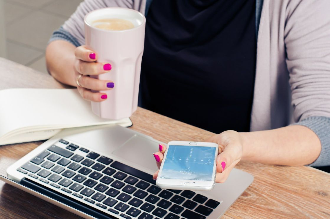 A student holding a phone in one hand and a cup of coffee in the other.