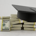 A stack of bills with a graduation cap sitting on top.