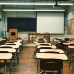 An empty classroom with a blackboard, as well as beige and brown desks.