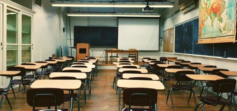 An empty classroom with a blackboard, as well as beige and brown desks.