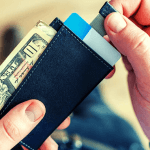 A student holding their wallet with a ten dollar bill sticking out of it.