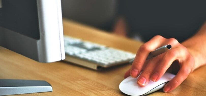 A student holding a mouse and a pen while sitting in front of a computer monitor.