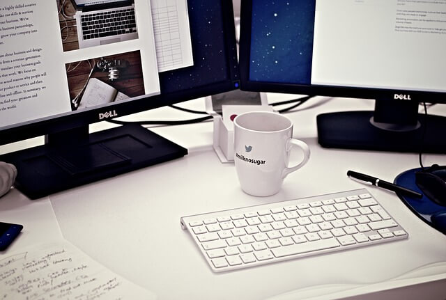 Dual Dell monitor on a desk with white coffee cup.