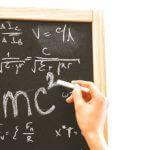A person writing math formulas on a chalkboard.