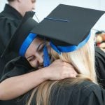 A graduating college student hugging another student.