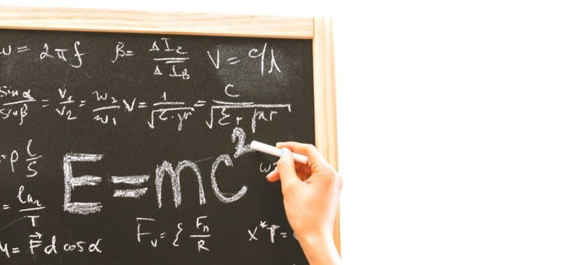 A person writing math formulas on a chalkboard.