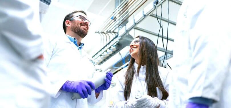 A group of scientists in white lab coats talking to each other.