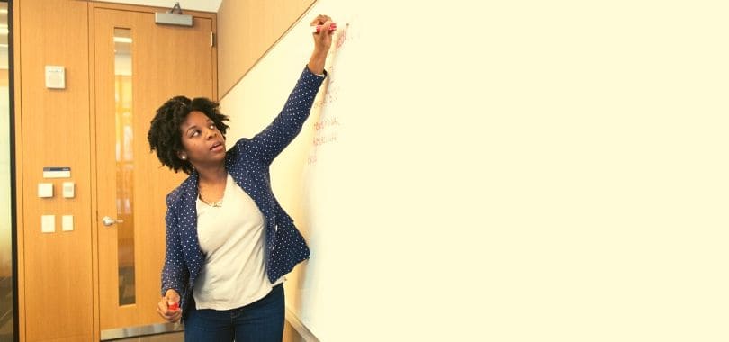 A person writing and talking up at a whiteboard.