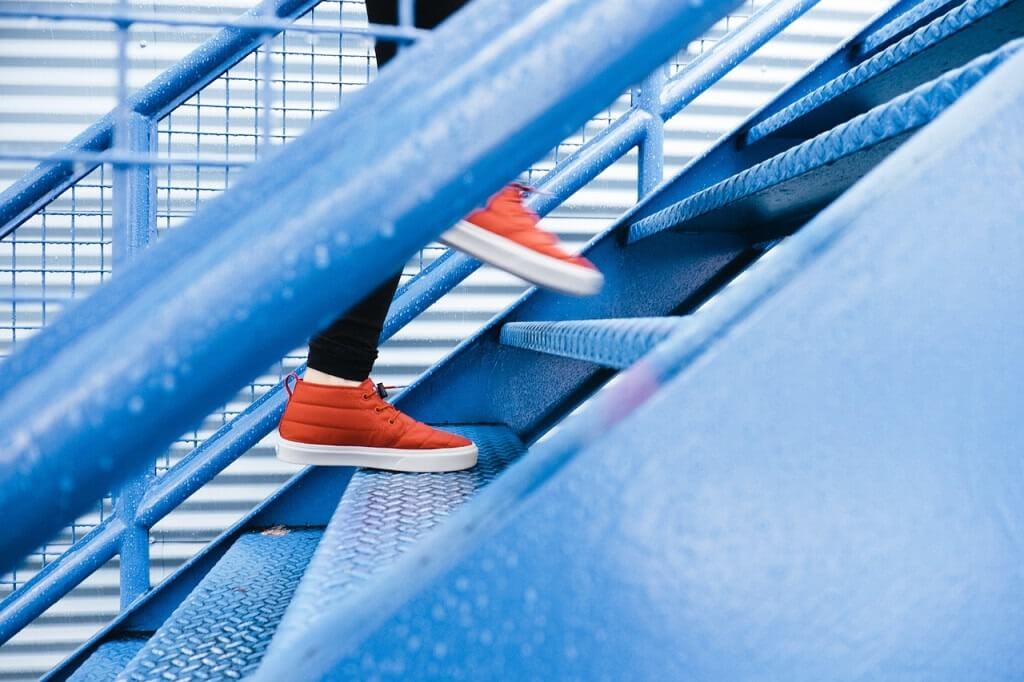 A person is wearing red shoes going up in a blue stair.
