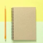 A pencil and notebook against a yellow and green background.