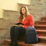 A student sitting on a staircase with a backpack next to them.
