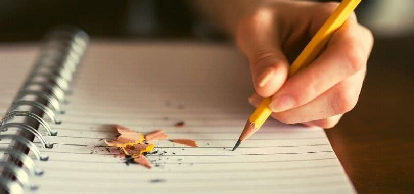 A student writes in a blank notebook while brainstorming their personal statement.