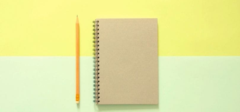 A pencil and notebook against a yellow and green background.