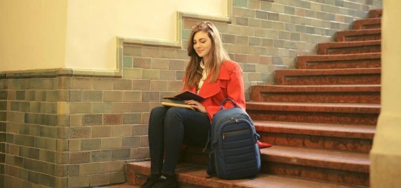 A student sitting on a staircase with a backpack next to them.