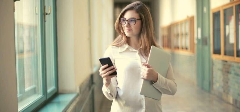 A student standing in a hallway holding a phone and folder.