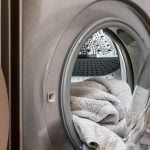 A silver washing machine with white towels inside the drum.