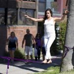 A girl walking on a purple tightrope that's tied to two trees.