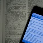 Cellphone with a dictionary app sitting on top of a physical dictionary.